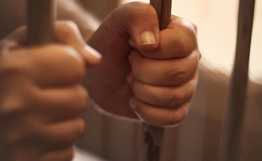 A man's hands tightly holding the bars of his jail cell.