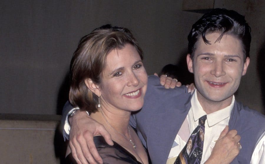 Carrie Fisher and Corey Feldman embrace for a picture at an event.