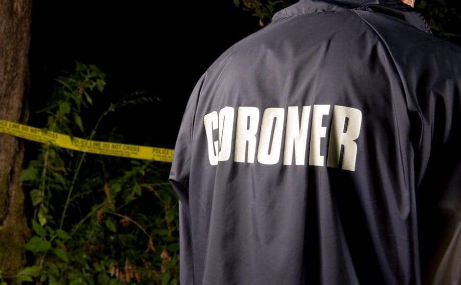 A coroner stands by a crime scene in the woods.