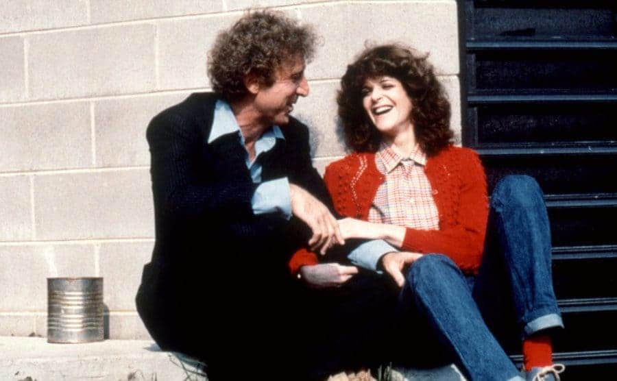 Gene and Gilda are sitting on the floor laughing.