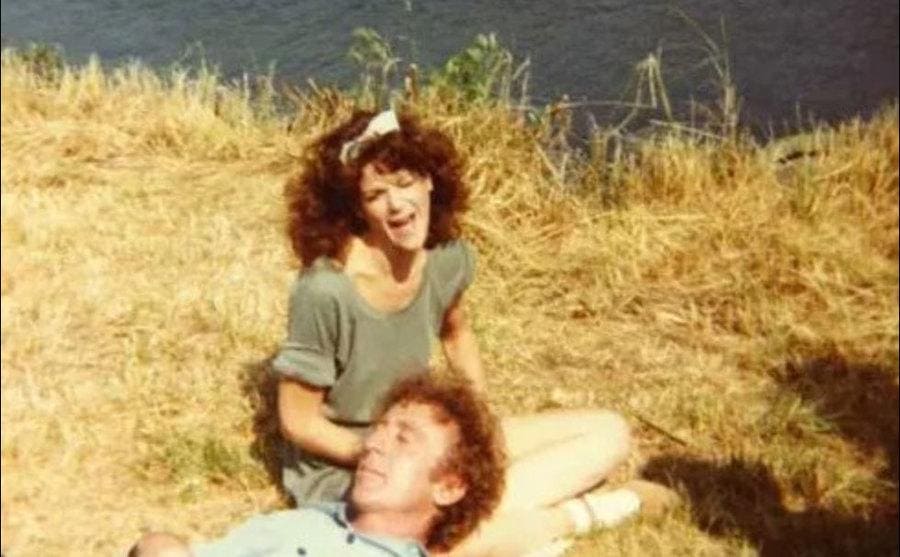 Gene is resting his head on Gilda’s lap as they sit by a lake.