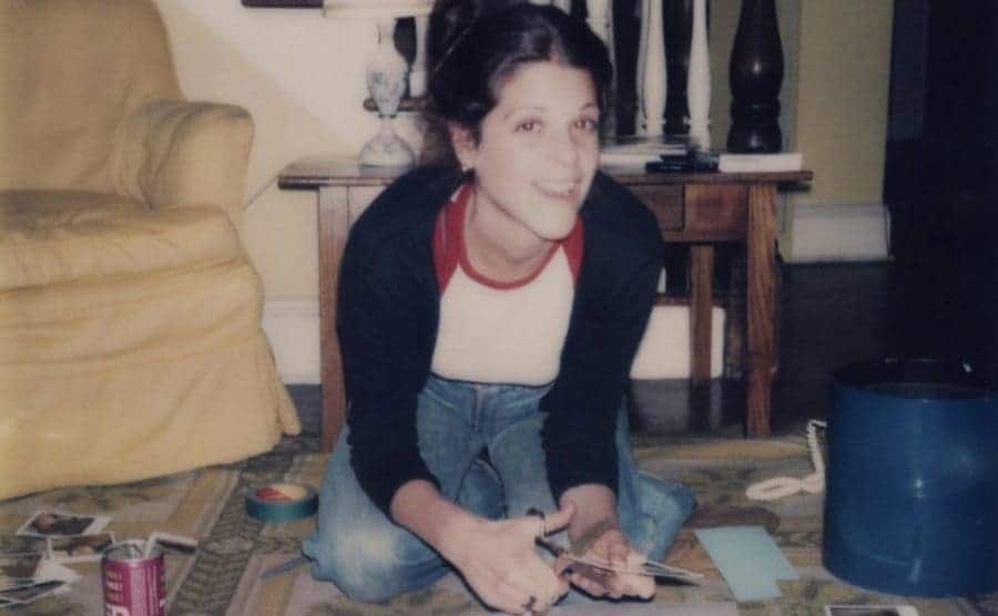Teenage Gilda is working on a scrapbook while sitting on the living room floor.