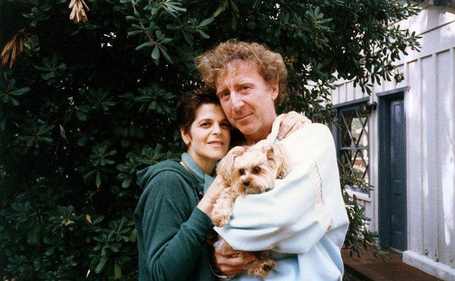 Gene and Gilda are embracing as they take a photo with their dog.