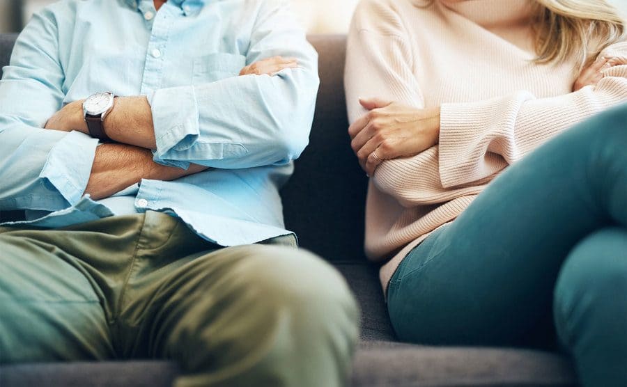 A couple is sitting on the sofa with their arms folded after an argument.