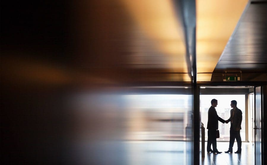 Two men are shaking hands in a corridor. 