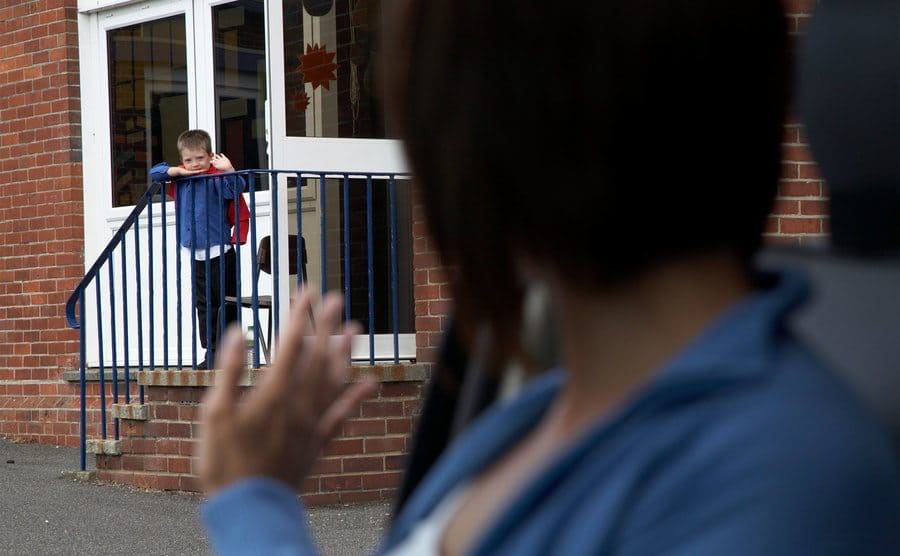 A little boy is waving goodbye to his mother in the car as she drops him off. 