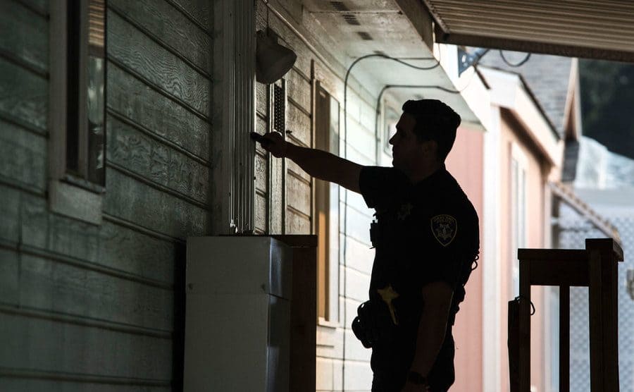 A police officer knocks on the front door of a residence. 