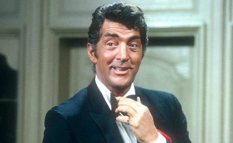 The entertainer Dean Martin is adjusting his bow tie on the set of the T.V show.