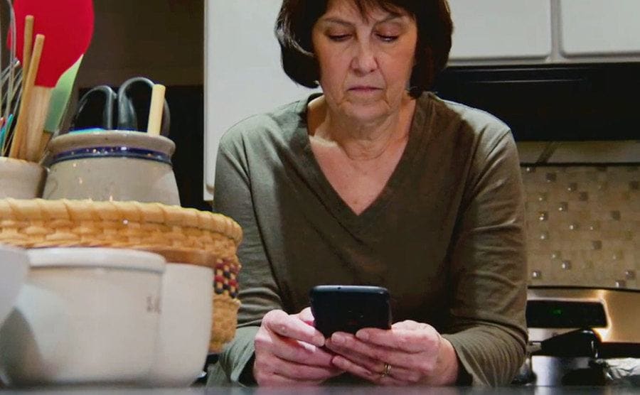 Raney is sitting next to the kitchen counter with her phone as she receives a message.
