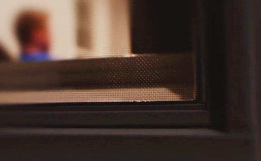 Looking in from the outside to the interior of Kroupa’s house while he sits watching T.V.