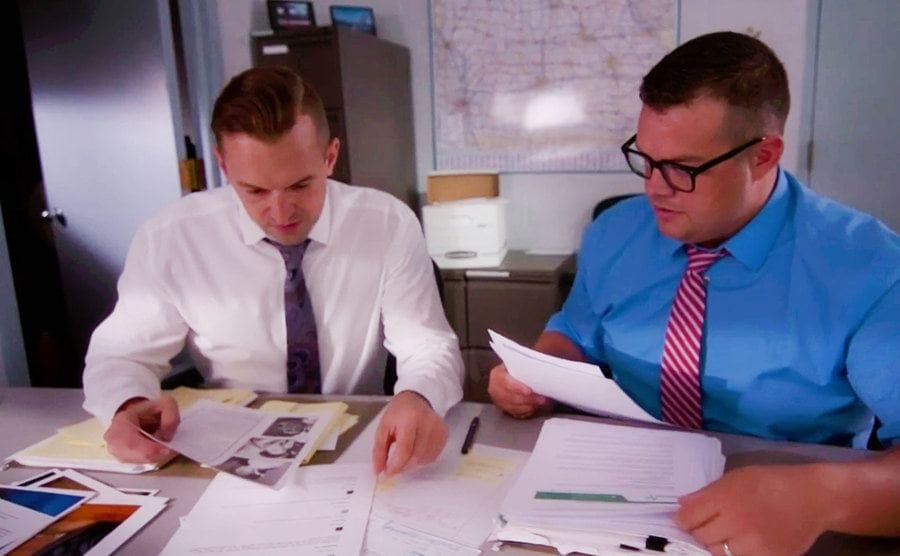Two investigators are sitting behind a desk, going through the evidence.
