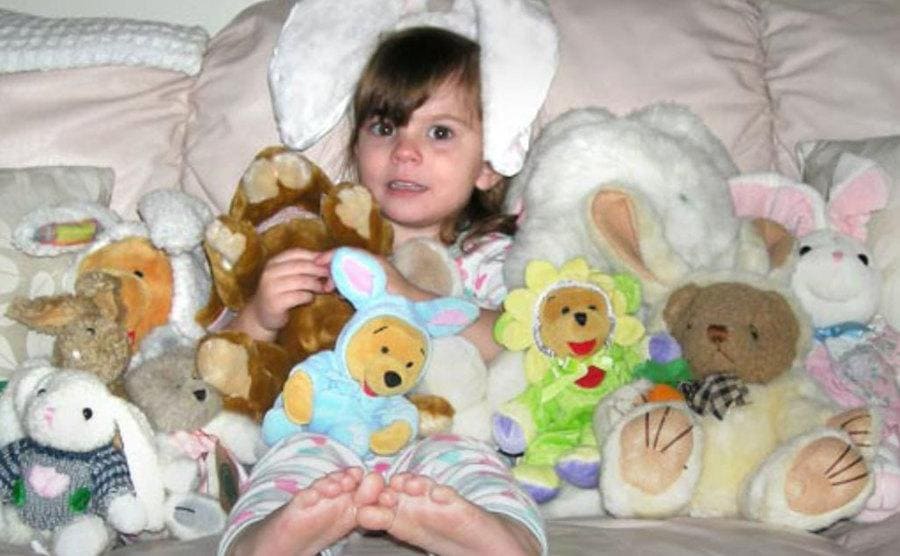 Caylee is sitting in bed surrounded by all her stuffed toys.
