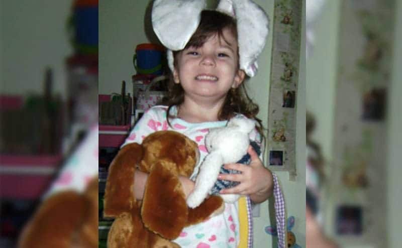 Cayley smiles at the camera while wearing big bunny ears and holding her stuffed animals.