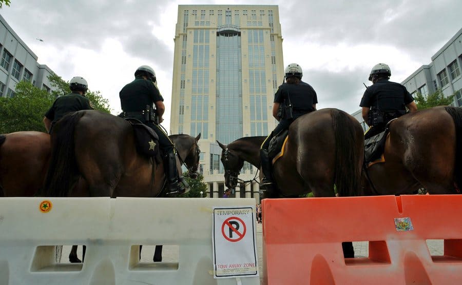 Four police officers on their horses are monitoring the protesters outside the courthouse.