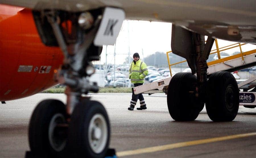 A luggage handler stands near a conveyor belt beside an aircraft.