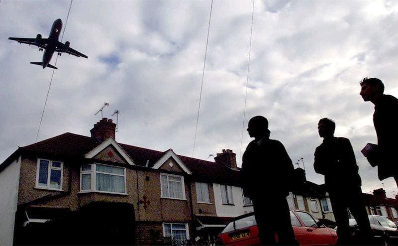 A plane flies overhead as bystanders lookup.