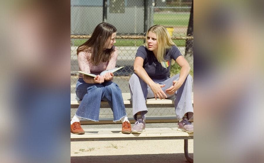 Linda Cardellini and Busy Philipps sit on the bleachers in a still from the show.