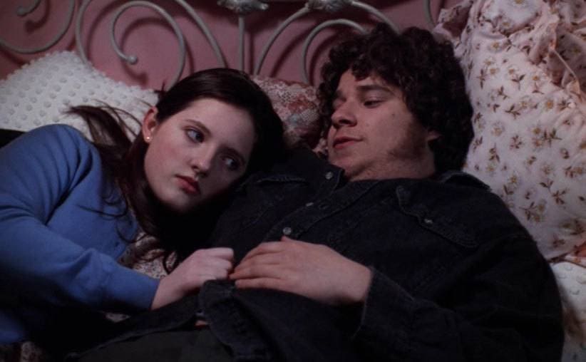 Rogen, as Ken, is in his girlfriend’s bed as they cuddle.