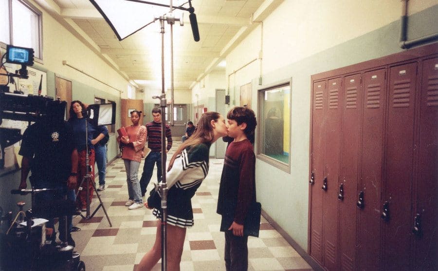 Camera crew film a scene where Sam receives a kiss from a cheerleader.