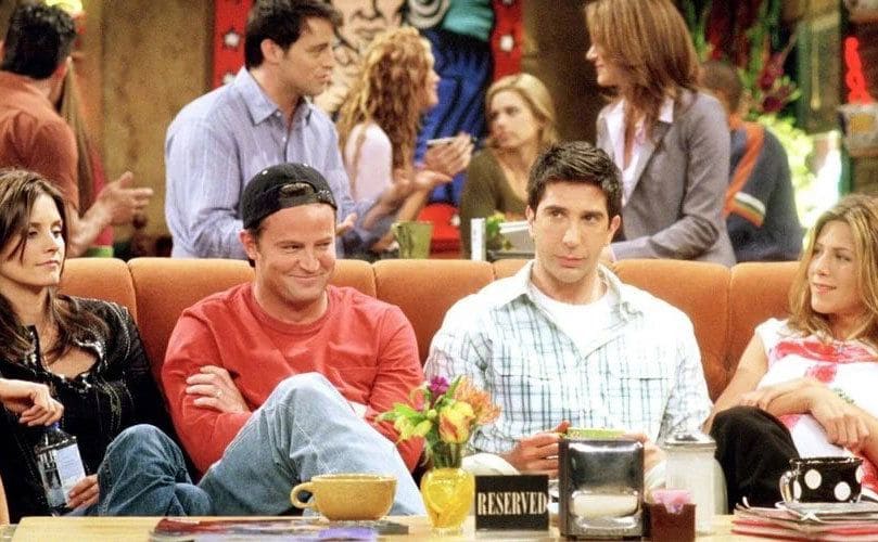 Monica, Chandler, Ross, and Rachel sit on the couch in Central Perk; you can spot the reserved sign on the coffee table.