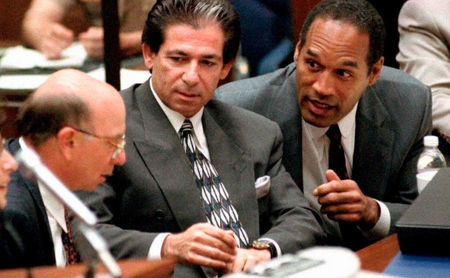 O.J. Simpson is consulting with his friend Robert Kardashian and his attorney during a hearing.