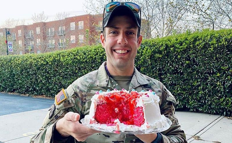 Kane holds a cake while smiling at the camera.