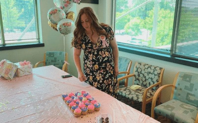 Chelsea is standing alone in her baby shower prepared by her co-workers.