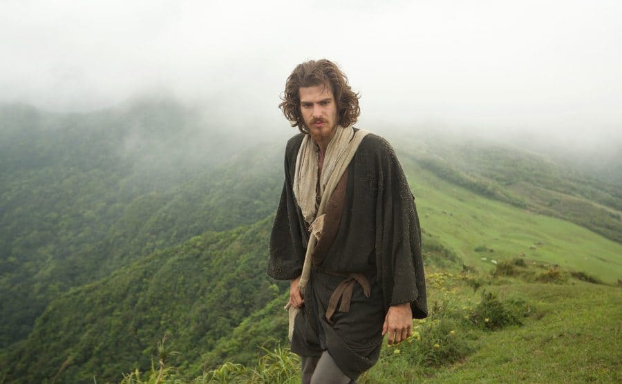 Andrew Garfield walks through the green mountains in the movie publicity still.