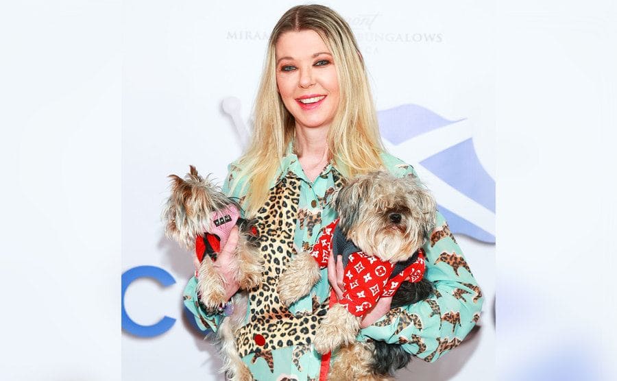 Tara Reid holds her two little dogs on each arm as she poses on the red carpet.
