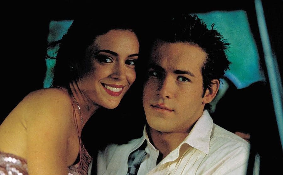 Alyssa Milano and Ryan Reynolds are sitting closely inside a car in a movie still.