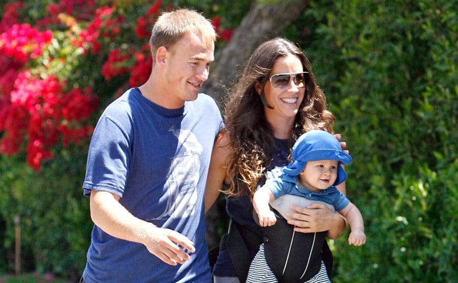 Alanis Morissette, Mario Treadway, and their baby boy Ever Imre are walking outside.