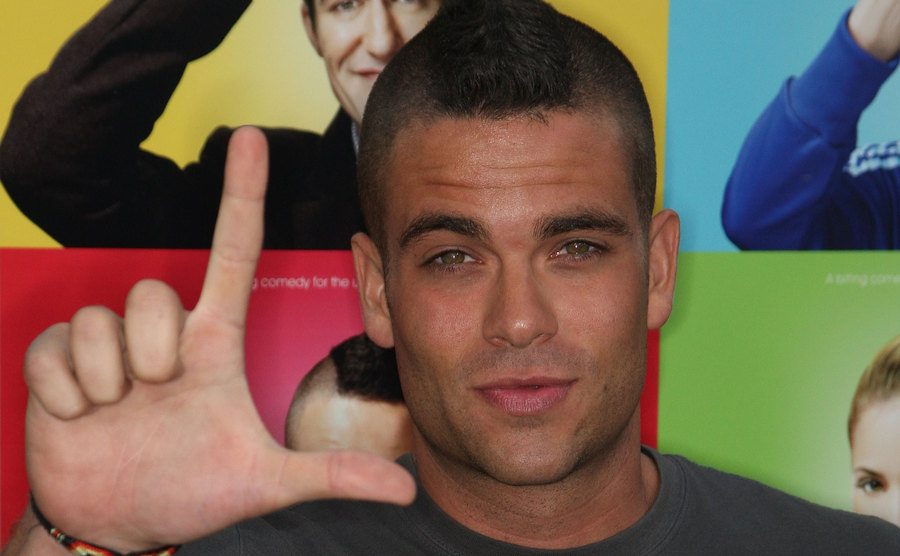 Mark Salling holding up an “L” sign with his fingers.