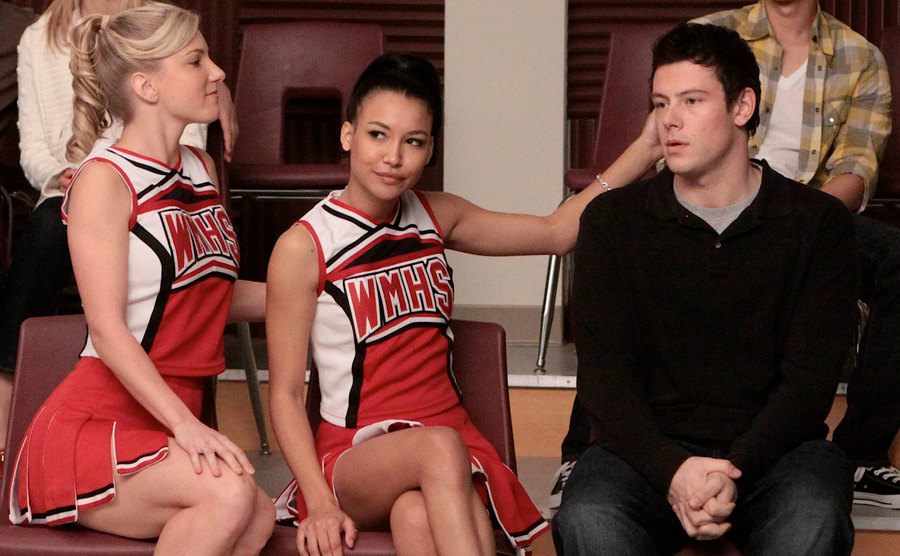 Heather Morris, Naya Rivera, and Cory Montieth are sitting on chairs on the set of Glee.