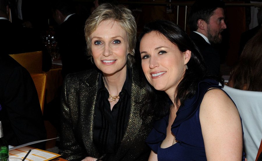 Jane Lynch and wife Lara Embry sitting at a table at an event.