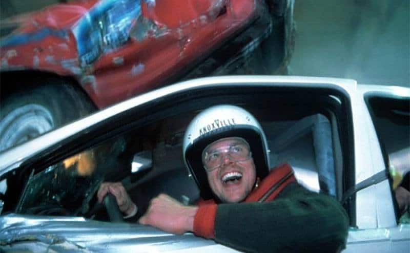 Johnny Knoxville sitting in a car and smiling as he looks out the window. 