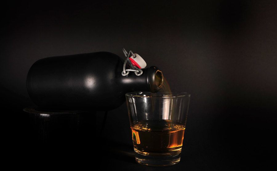 A black bottle and a glass of whiskey.