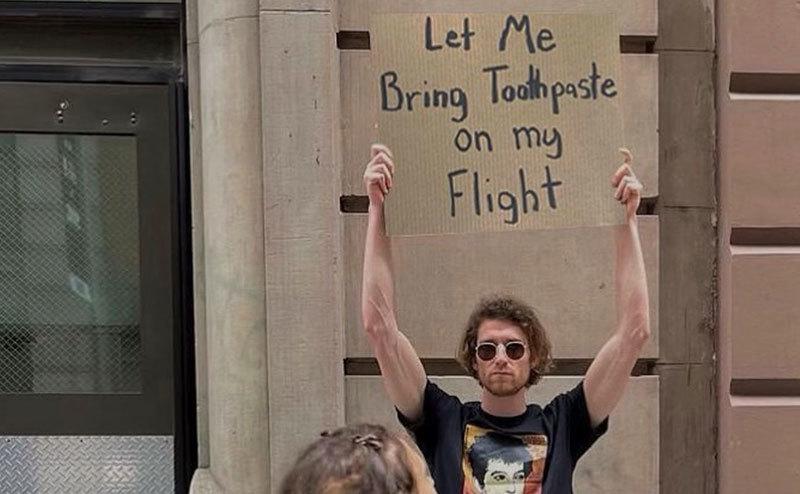 A man is holding a sign that reads, ‘’Let Me Bring Toothpaste on My Flight.’’