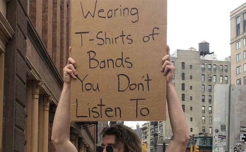 A man is holding a sign that reads ‘’Stop Wearing T-Shirts of Bands You Don’t Listen to.’’