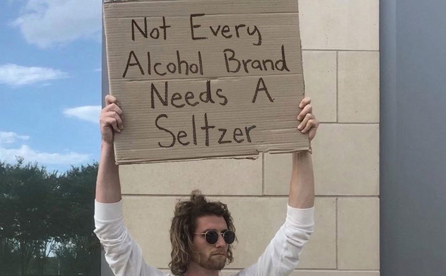 A man is holding a sign that reads ‘’Not Every Alcohol Brand Needs a Seltzer.’’