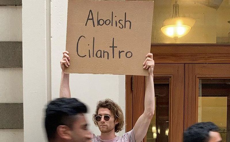 A man is holding a sign that reads ‘’Cilantro Should be Abolished.’’