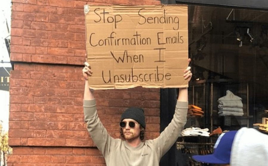 A man is holding a sign that reads ‘’Stop Sending Confirmation Emails when I Unsubscribe.’’