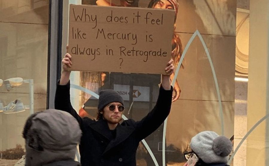 A man is holding a sign that reads ‘’Why Does it Feel Like Mercury is Always in Retrograde?’’
