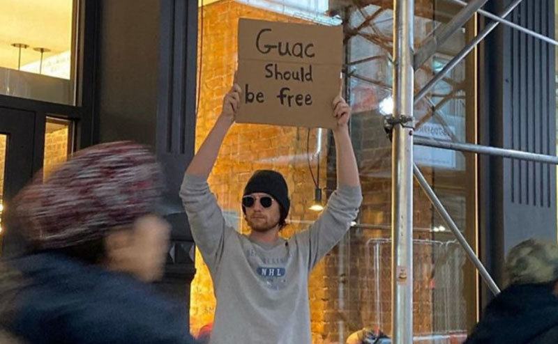 A man is holding a sign that reads ‘’Guac Should be Free.’’