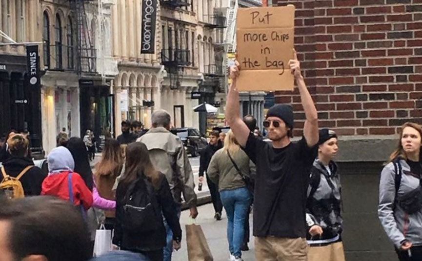 A man is holding a sign that reads ‘’Put More Chips in the Bag.’’