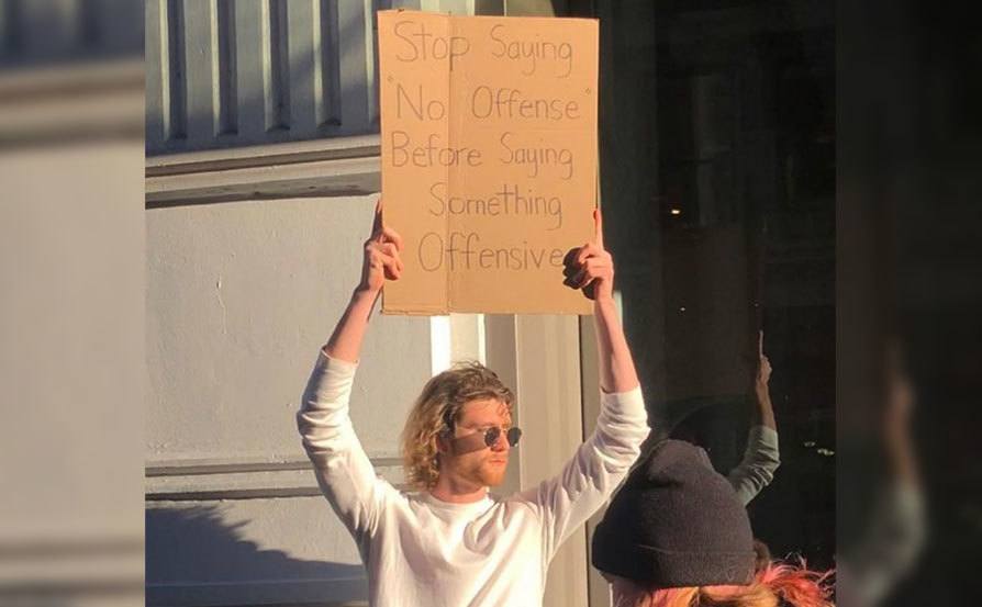 A man is holding a sign that reads ‘’Stop Saying No Offense Before Saying Something Offensive.’’