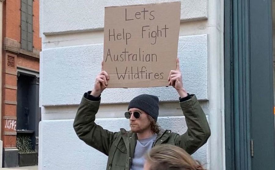 A man is holding a sign that reads ‘’Let’s Help Fight Australian Wildfires.’’