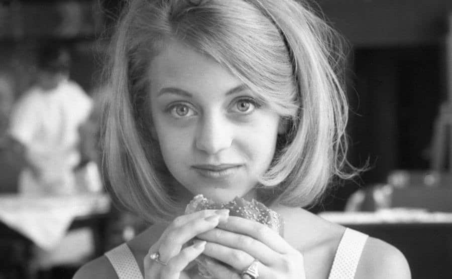Goldie Hawn sits in a restaurant with a hamburger in her hands.