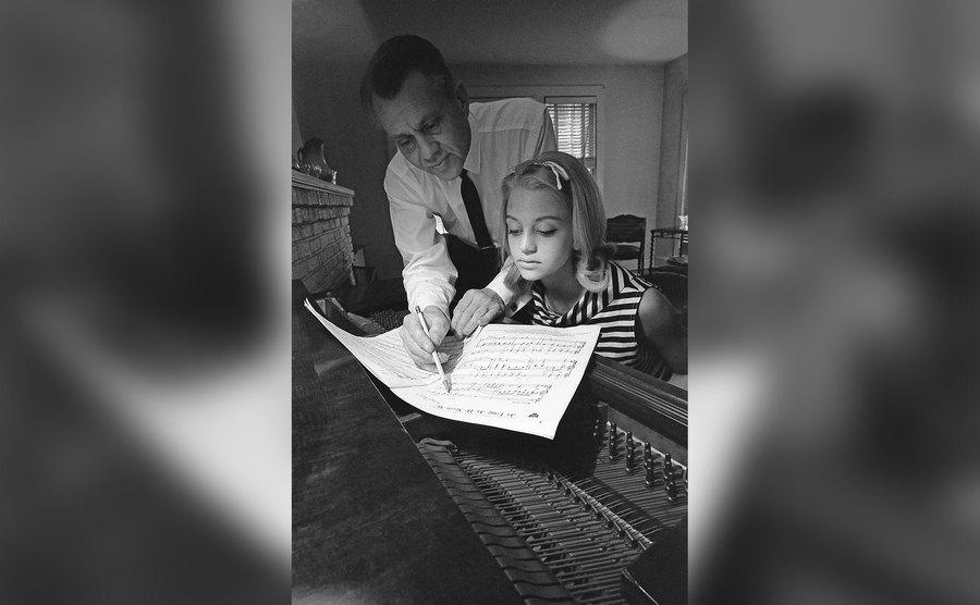 Goldie Hawn looks over sheet music at the piano with her father.