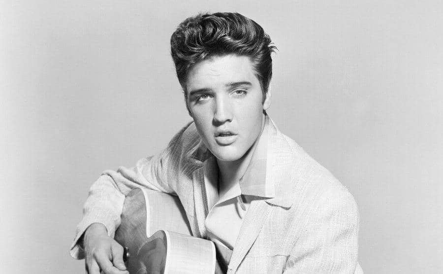 Elvis Presley strums his acoustic guitar in a portrait.