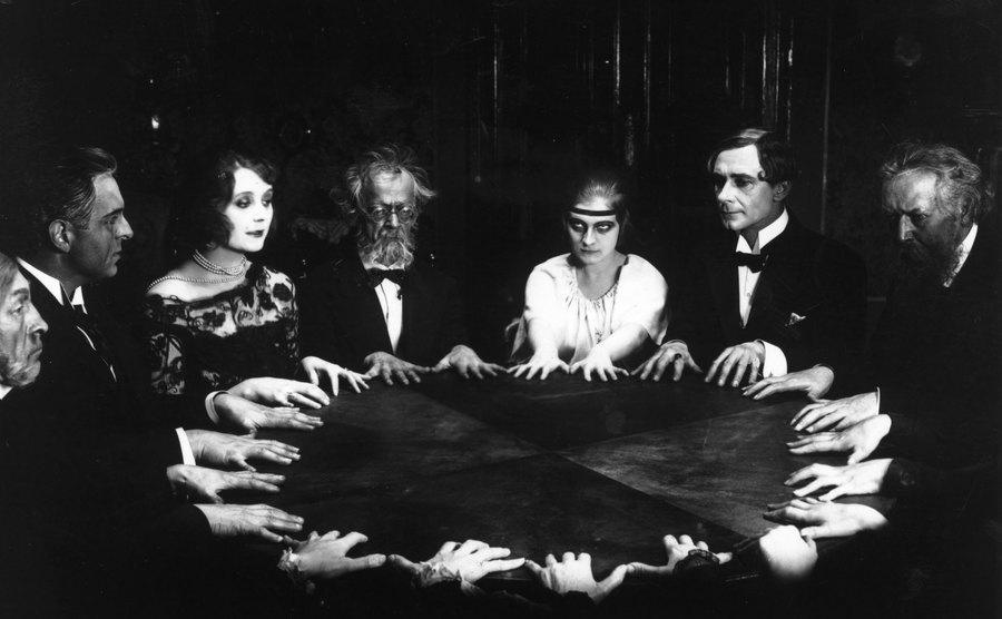 A circle of people at a spirited meeting joining hands around a table.